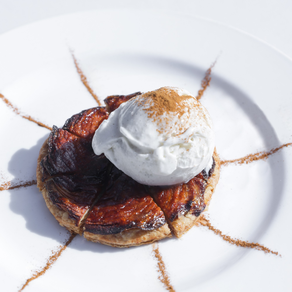 Caramelized apple tart with a scoop of vanilla ice cream and cinnamon dust on a white plate.