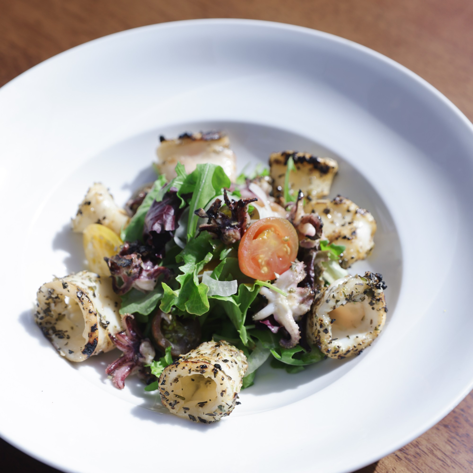Grilled calamari salad with mixed greens and cherry tomatoes in a white bowl at Cafe Santorini.