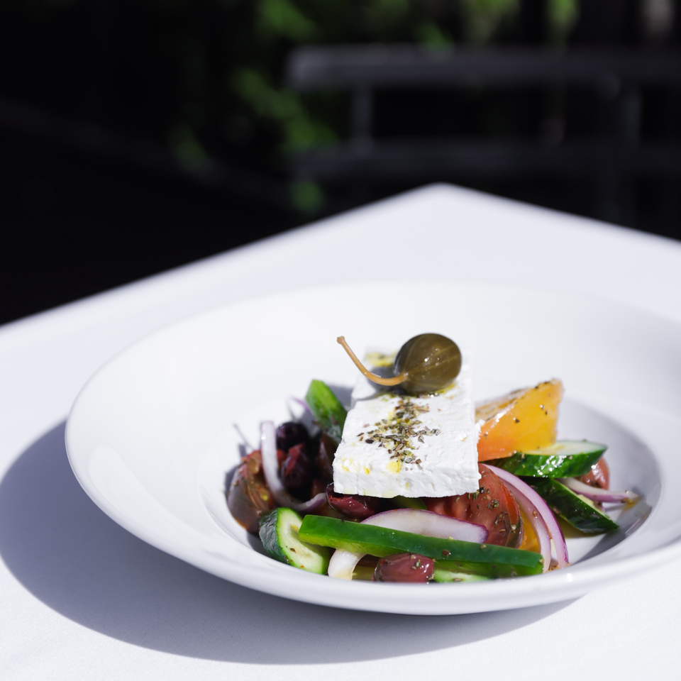A Mediterranean salad with feta, tomatoes, cucumbers, onions, olives, and a caper berry.